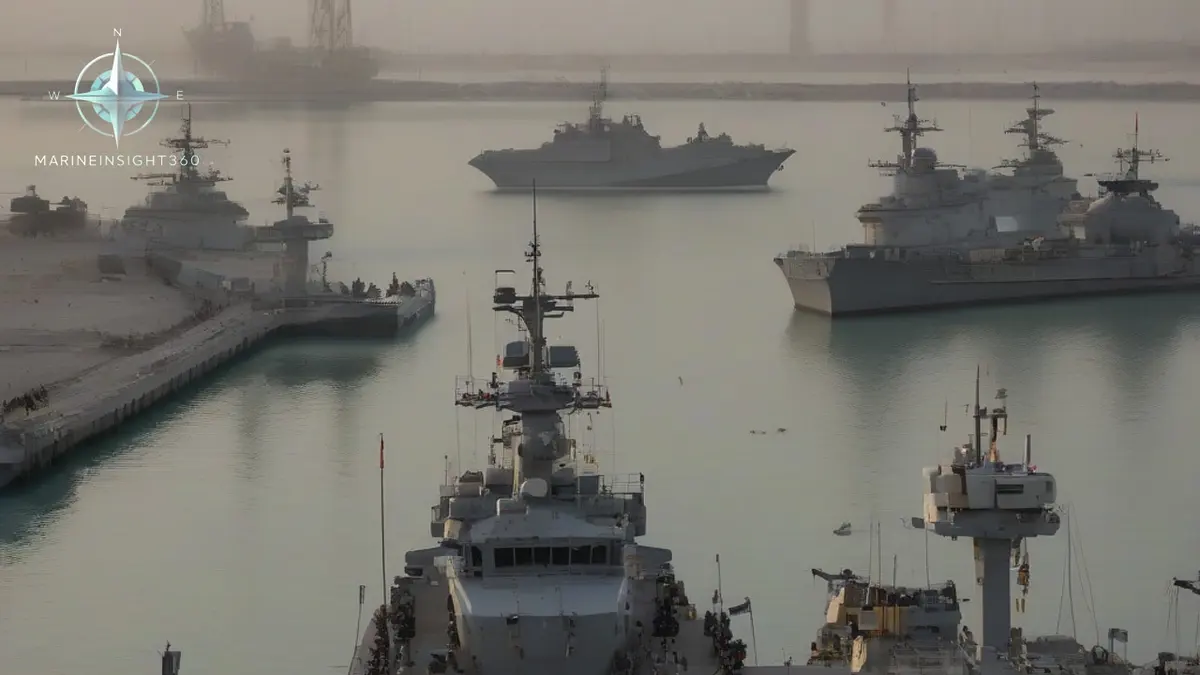 Grey warships berthed at a Bahrain naval base at dawn behind boom defence floats